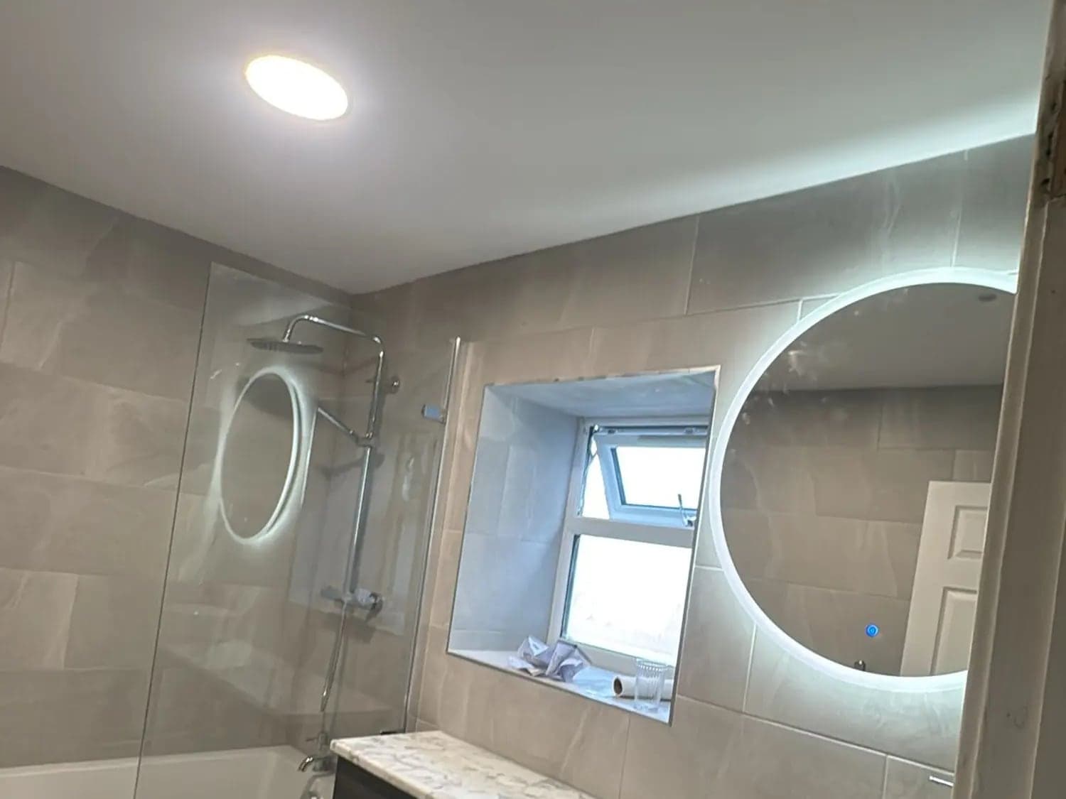 Bathroom with a ceiling downlight, a backlit round mirror and a lit shower mirror